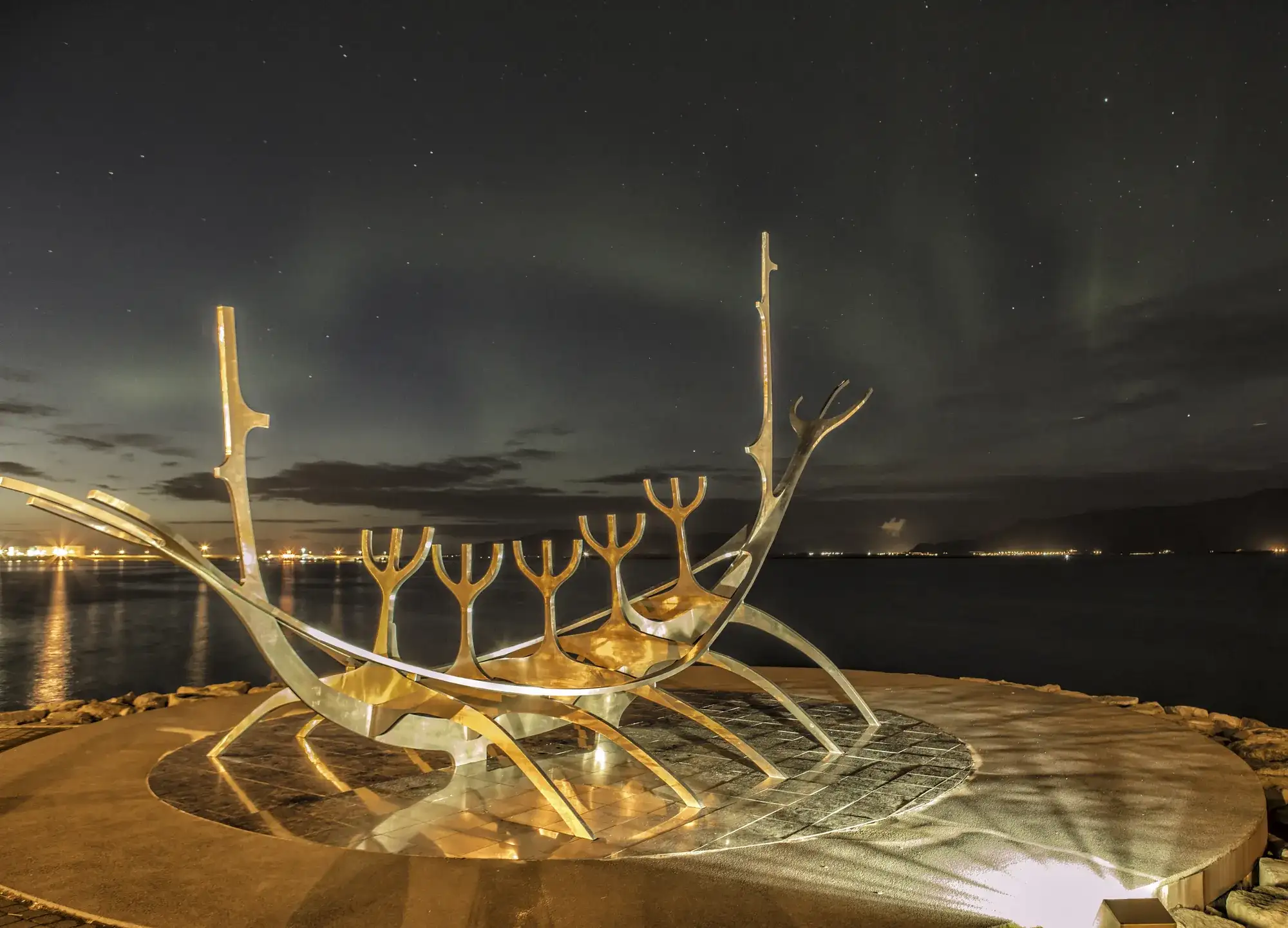 The Sun Voyager sculpture lit at night on the Reykjavík waterfront under a faint aurora.