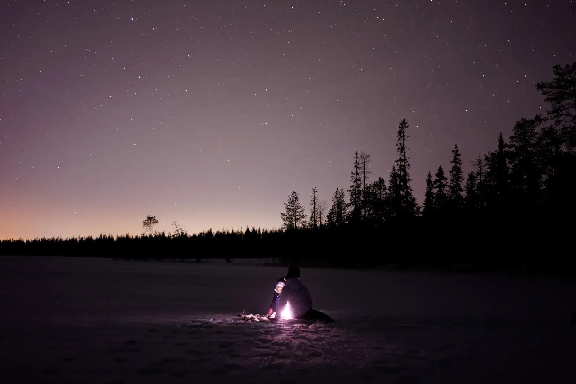 A small figure with a glowing lantern on a snowfield at dusk near Rovaniemi.